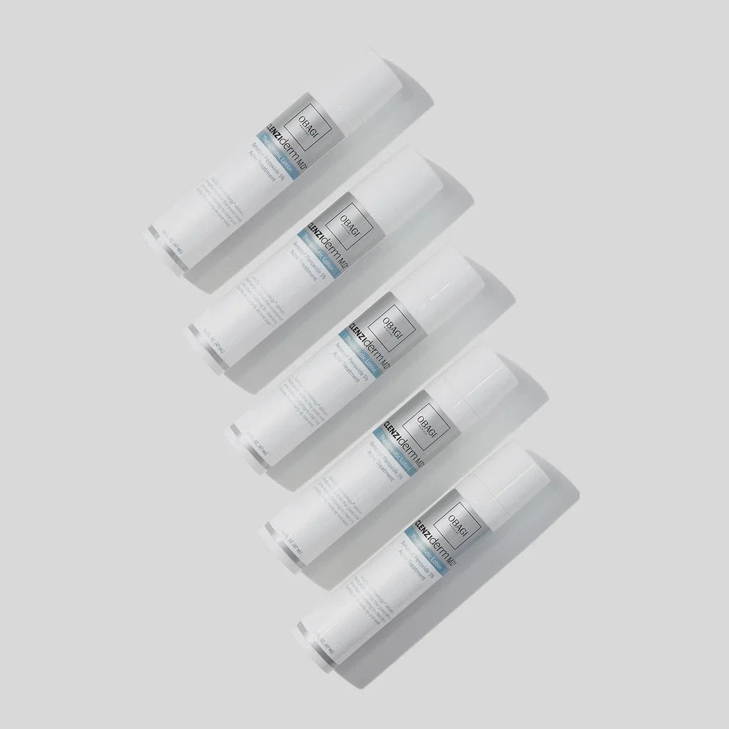 Five white cylindrical cosmetic tubes arranged diagonally on a light gray background. Each tube has a white cap, a white body with a silver-gray label, and a thin blue accent line near the top of the label.