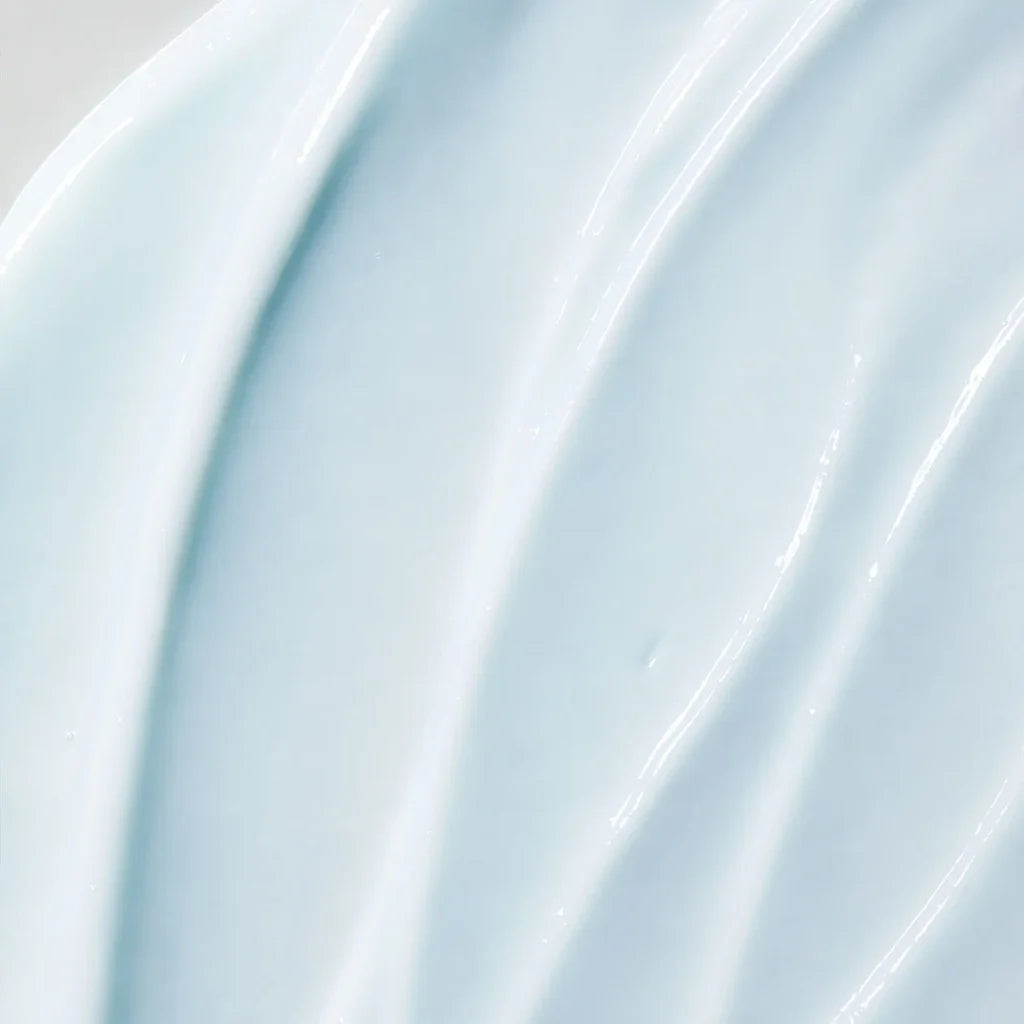 A close-up texture shot of a smooth, glossy, pale icy blue cream or gel with soft diagonal ridges.