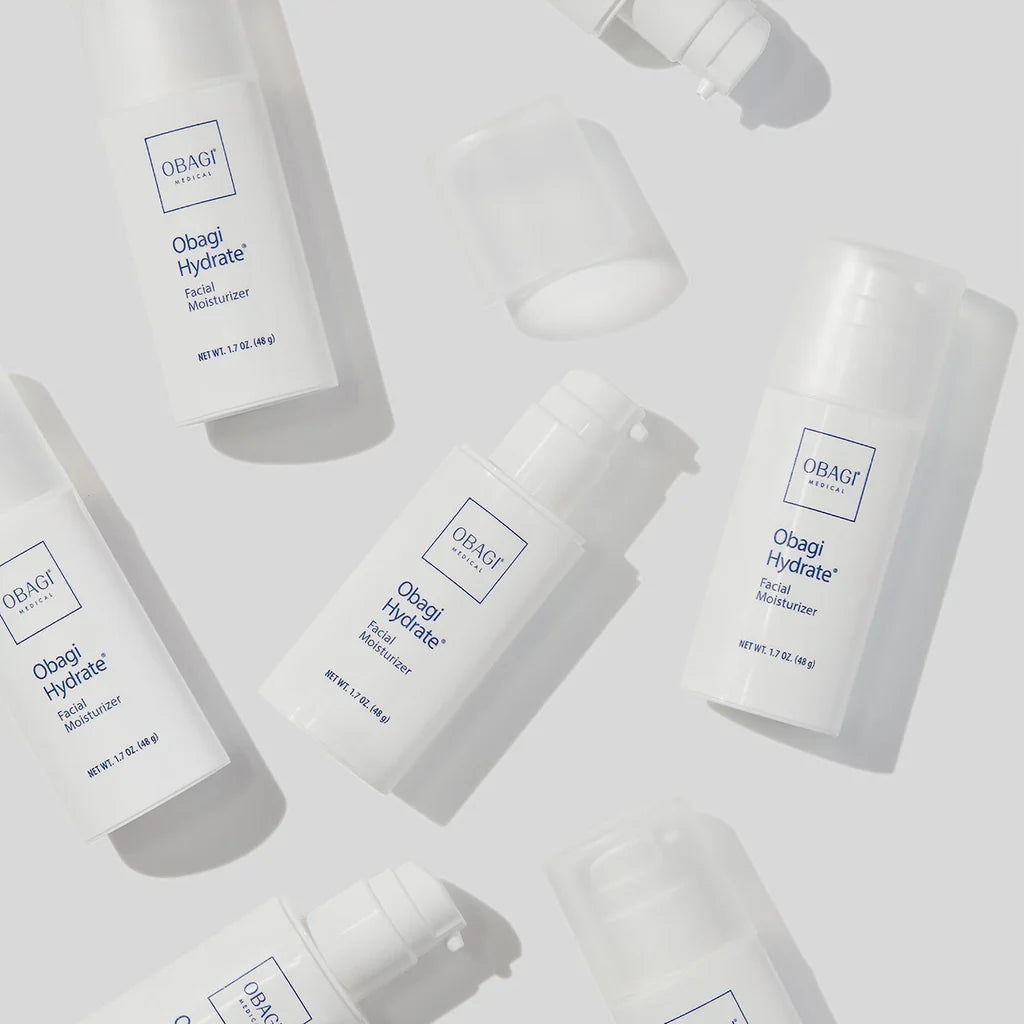 Several white Obagi Hydrate Facial Moisturizer bottles and pump containers arranged on a light gray background with soft shadows.