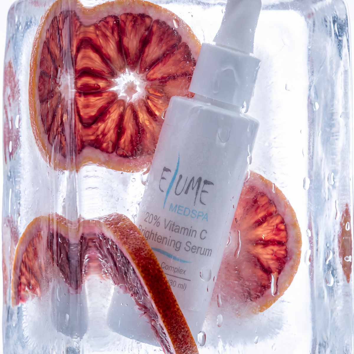 A white dropper bottle of Eume Medspa Vitamin C Brightening Serum, partially submerged inside a clear ice cube with sliced red blood oranges visible through the transparent block.