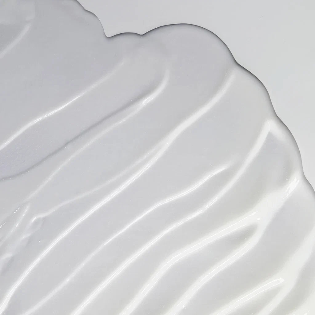 A close-up of a smooth, glossy white cosmetic cream or gel swatch with soft diagonal ridges on a light gray background.