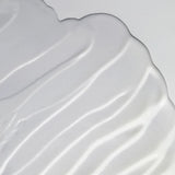 A close-up of a smooth, glossy white cosmetic cream or gel swatch with soft diagonal ridges on a light gray background.