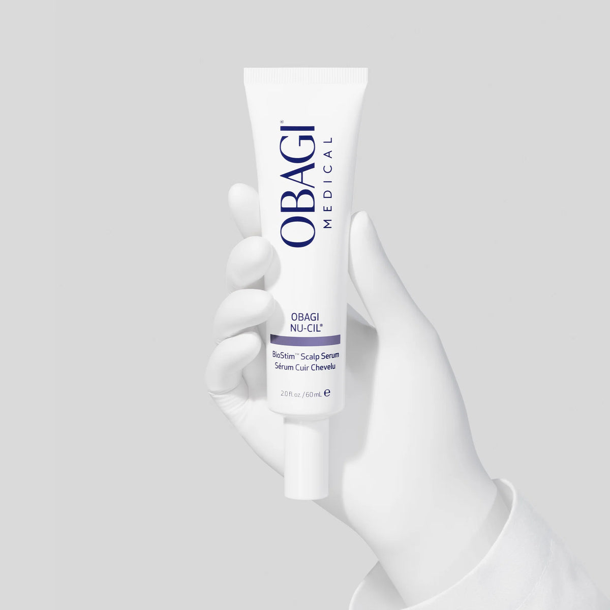 A white Obagi Medical serum tube held by a white gloved hand against a light gray background.