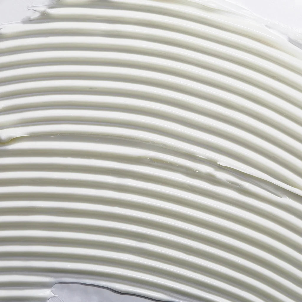 A close-up texture shot of a thick, creamy off-white cosmetic cream with horizontal ridges.