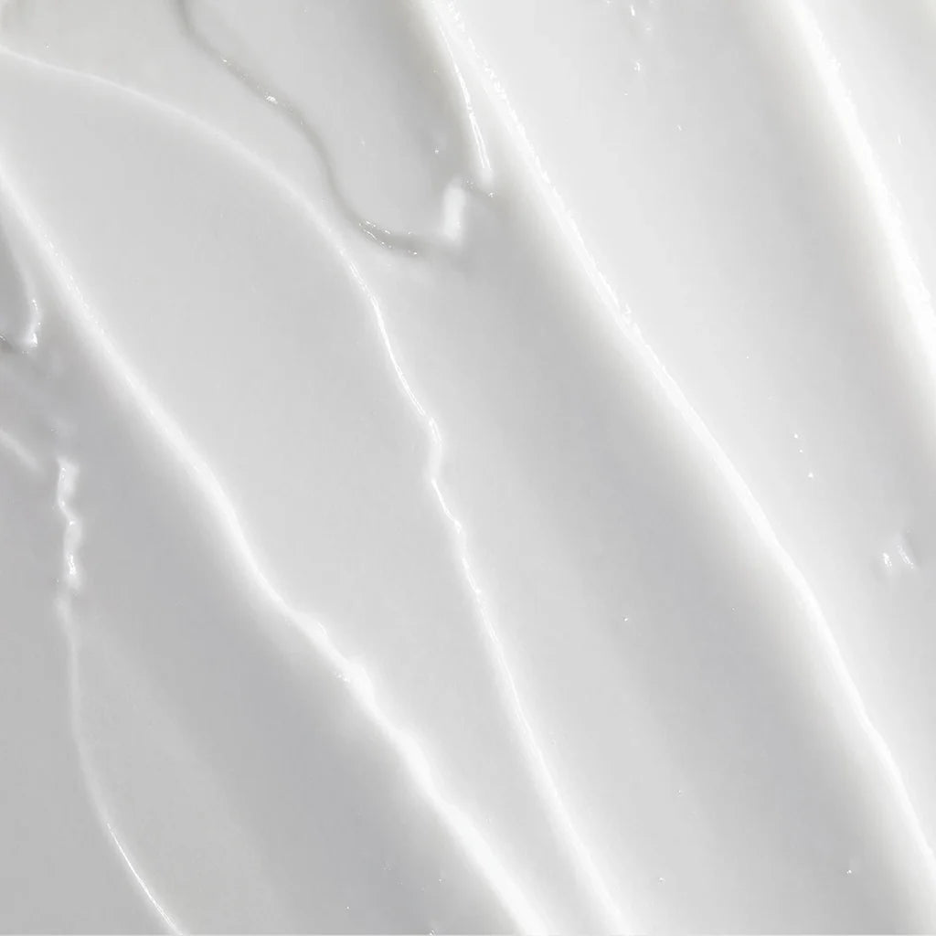 A close-up texture shot of a thick, creamy white cosmetic cream with soft diagonal swirled lines and subtle highlights.