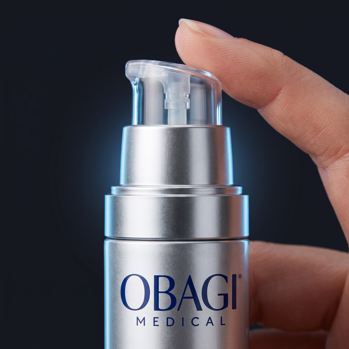 A close-up of a silver Obagi Medical skincare pump bottle being held by a hand against a dark background.