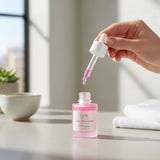 Elume Med Spa Lactic Acid Resurfacing Serum in a pink glass bottle with a dropper being held over a bathroom counter.