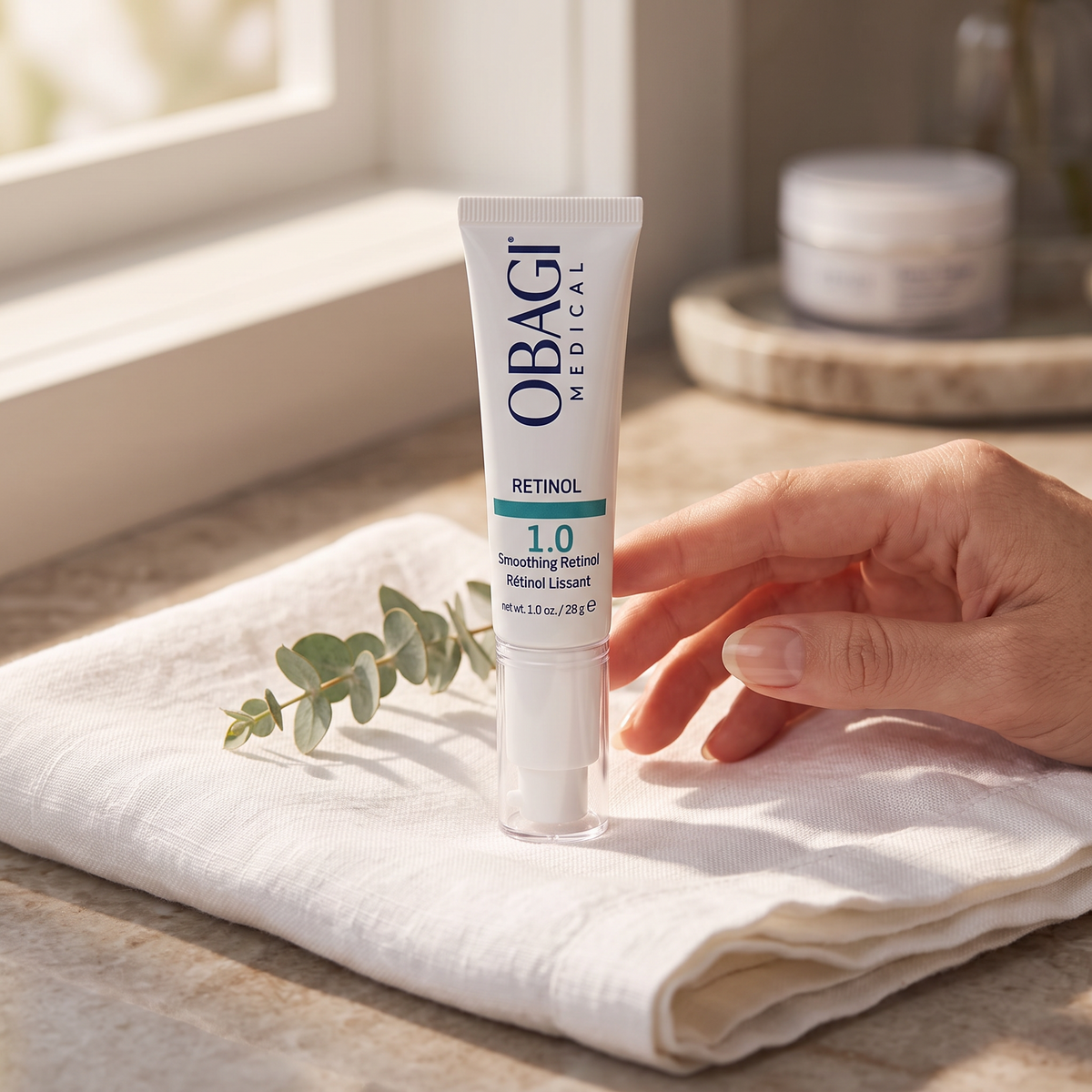 Elume Medspa Obagi Retinol 1.0 anti-aging serum tube resting on a white cloth with a sprig of eucalyptus