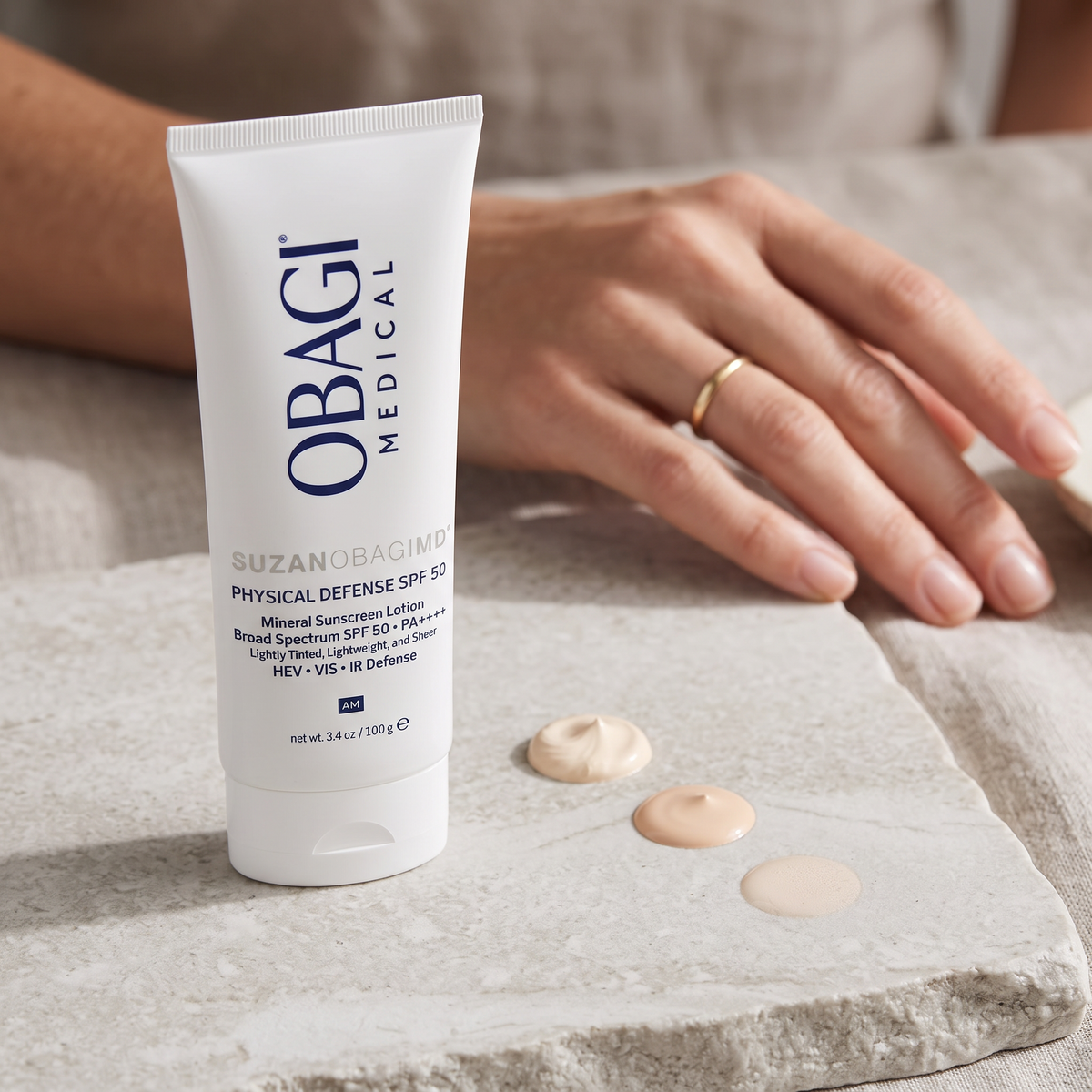 Elume Medspa SUZANOBAGIMD Tinted Physical Defense SPF 50 sunscreen tube with three shades of tinted lotion swatches.