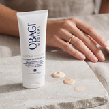 Elume Med Spa SUZANOBAGIMD Tinted Physical Defense SPF 50 sunscreen tube with three shades of tinted lotion swatches.